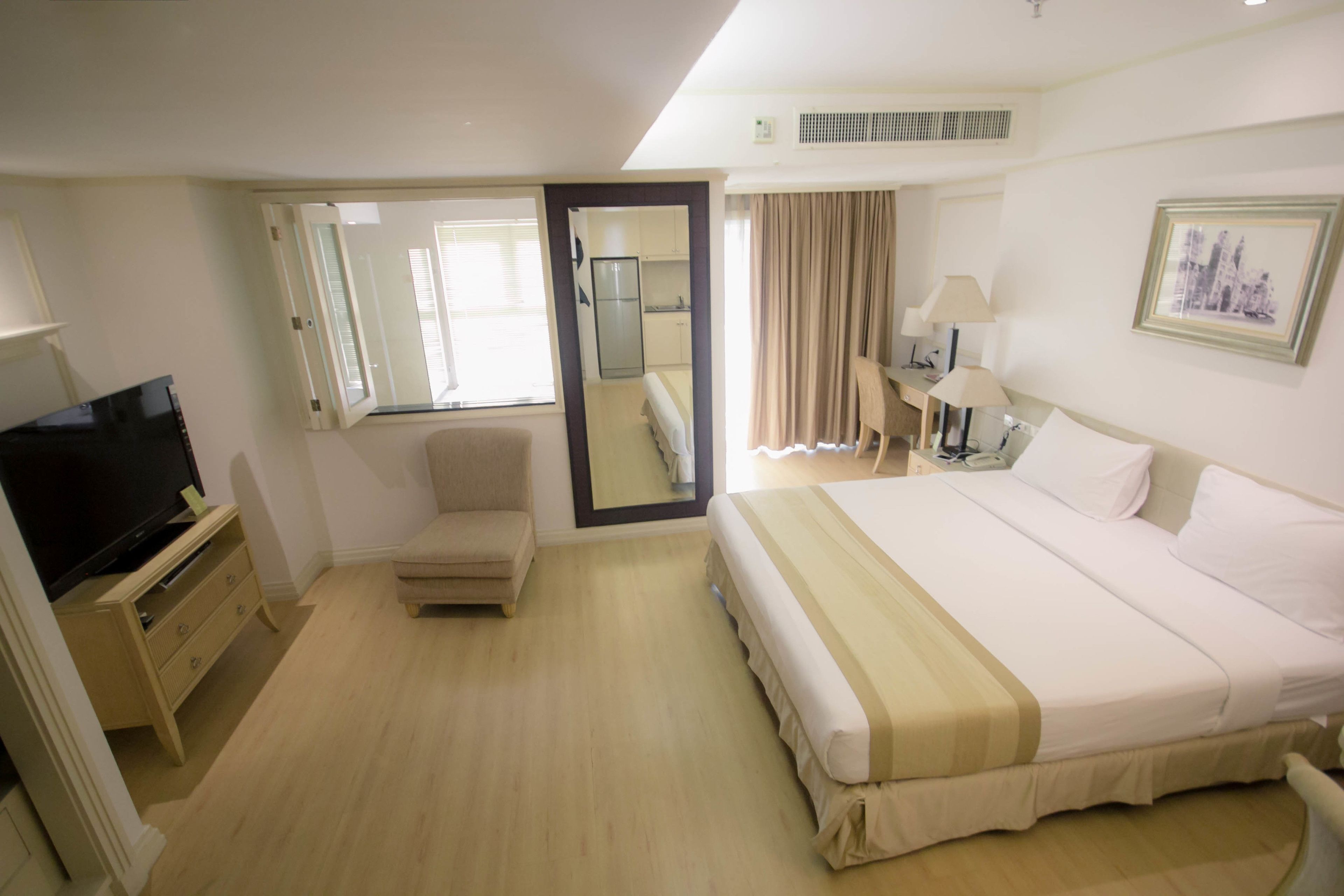 A hotel room with a bed, a television, a desk, a chair, and a mirror.