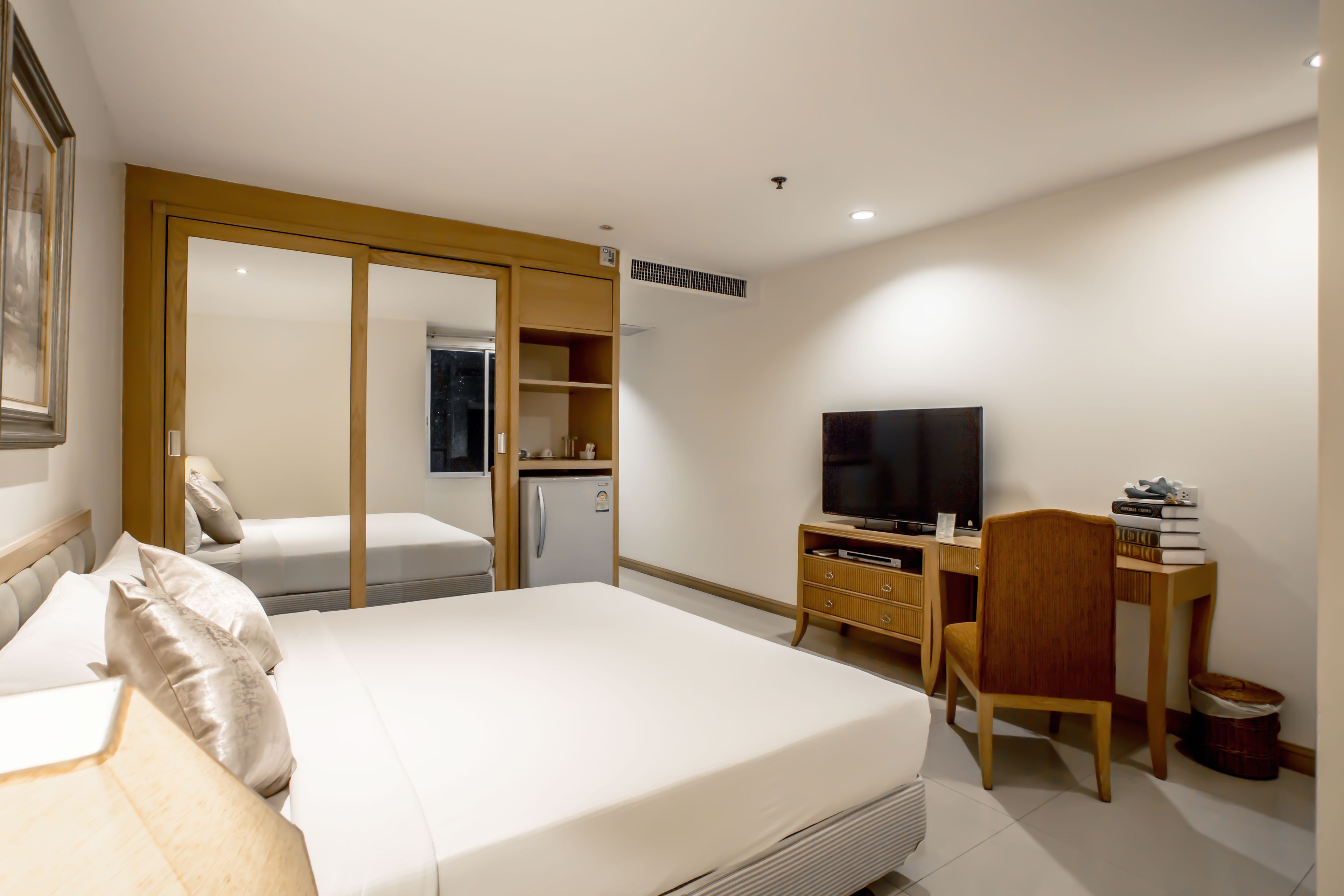 A modern hotel room with a bed, a desk, a television, and a wardrobe.