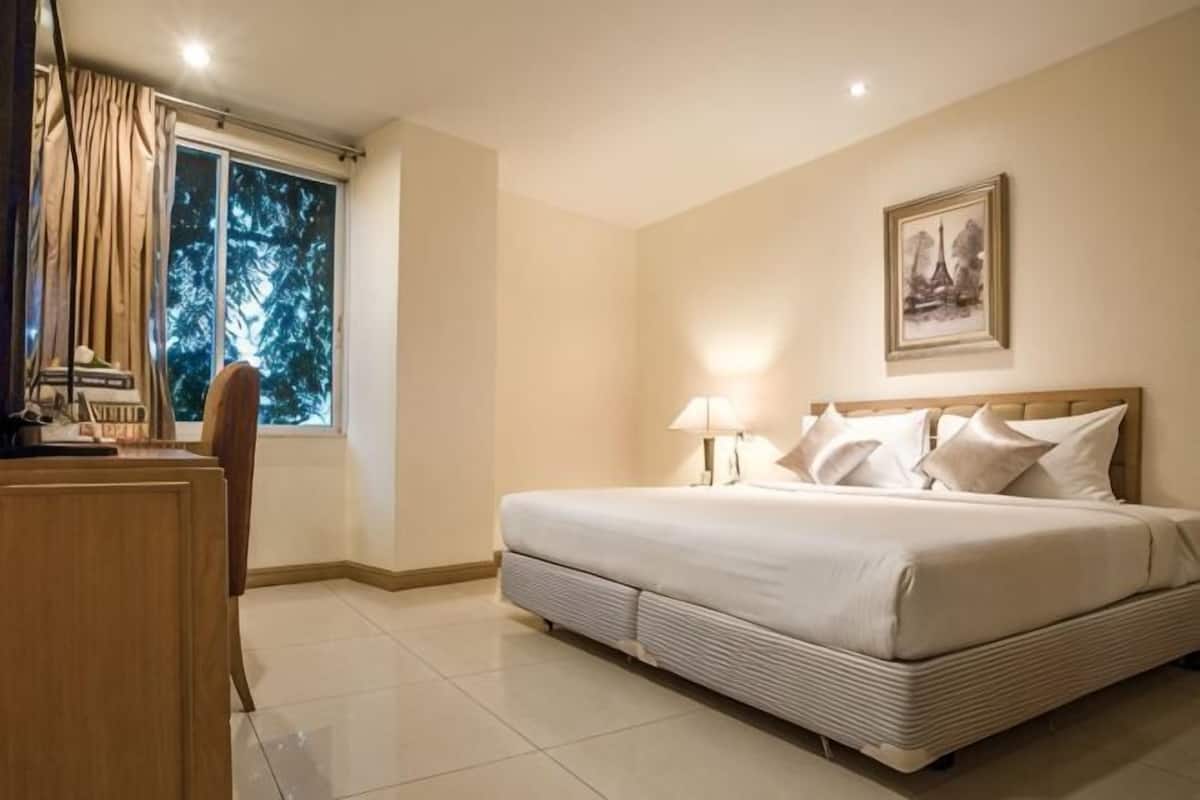 A hotel room with a bed, a desk, a chair, a window with curtains, and a wall-mounted picture.