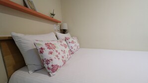 A neatly made bed with white bedding and floral-patterned pillows. - Just4U (Seoul)