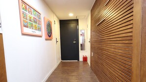 A hallway with wooden flooring, a black door, and framed artwork on the walls. - Just4U (Seoul)
