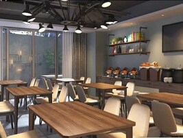Un espace repas moderne avec des tables et des chaises en bois, de grandes fenêtres et un coin cuisine doté d’étagères et d’appareils électroménagers.