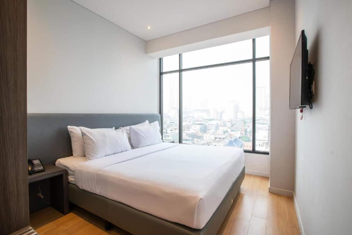 Een moderne hotelkamer met een groot bed, een nachtkastje met telefoon en een aan de muur bevestigde televisie.