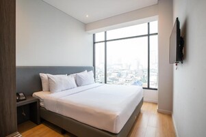 Una habitación de hotel moderna con una cama grande, una mesita de noche con teléfono y un televisor montado en la pared.