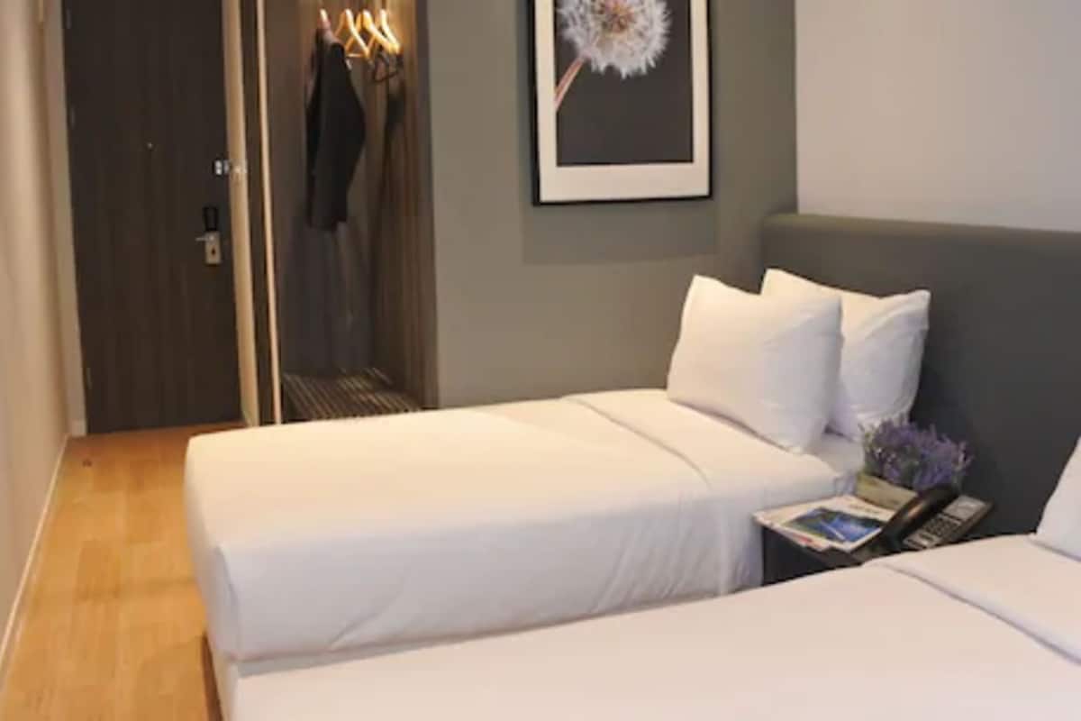 Een hotelkamer met een bed, nachtkastje met telefoon en tijdschrift, kast met kleren en een foto in een lijst aan de muur.
