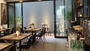 A restaurant with multiple tables and chairs, large windows, and a bar area with bottles. - Juno Tanah Abang Jakarta (Jakarta)