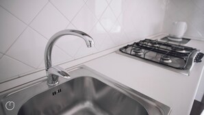 A stainless steel kitchen sink with a modern faucet, a gas stove, and white tiled backsplash. - Italianway   - Giulio Romano (Milan)