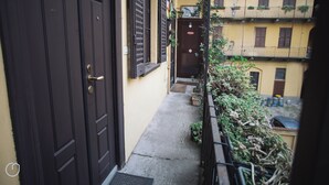 A narrow alleyway with a dark brown door on the left and a yellow building with balconies on the right. - Italianway   - Giulio Romano (Milan)