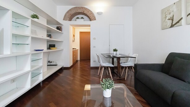 A modern living room with a dining area, white shelving, a dark sofa, and a small table with a plant. - Italianway   - Giulio Romano (Milan)