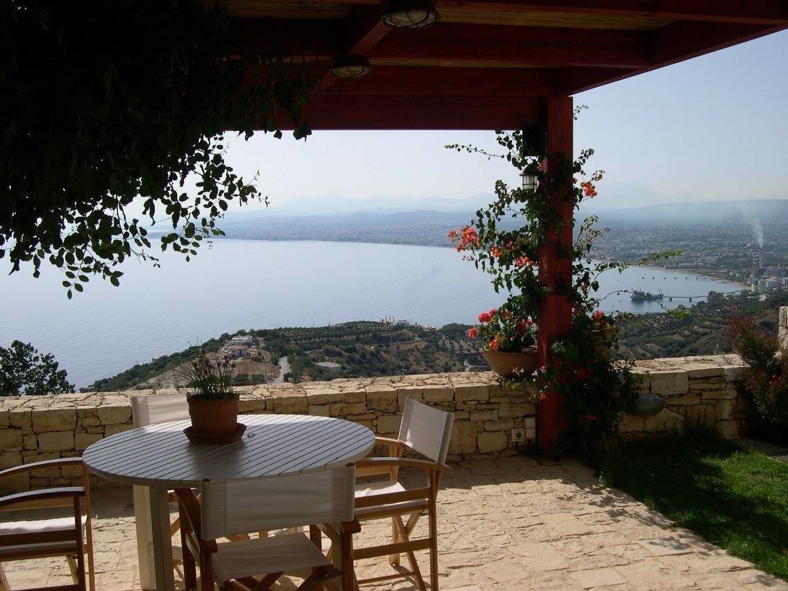 A patio with a round table and chairs, overlooking a body of water and a distant cityscape.