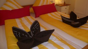 A hotel room with two beds, each with striped bedding and red pillows. There is a nightstand with a lamp and a small drawer.
