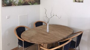 A dining area with a wooden table, four chairs, a vase with branches, and a painting of a waterfall.