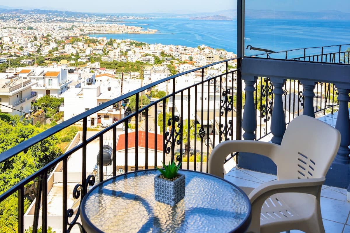 A balcony with a table and chairs, overlooking a coastal cityscape.
