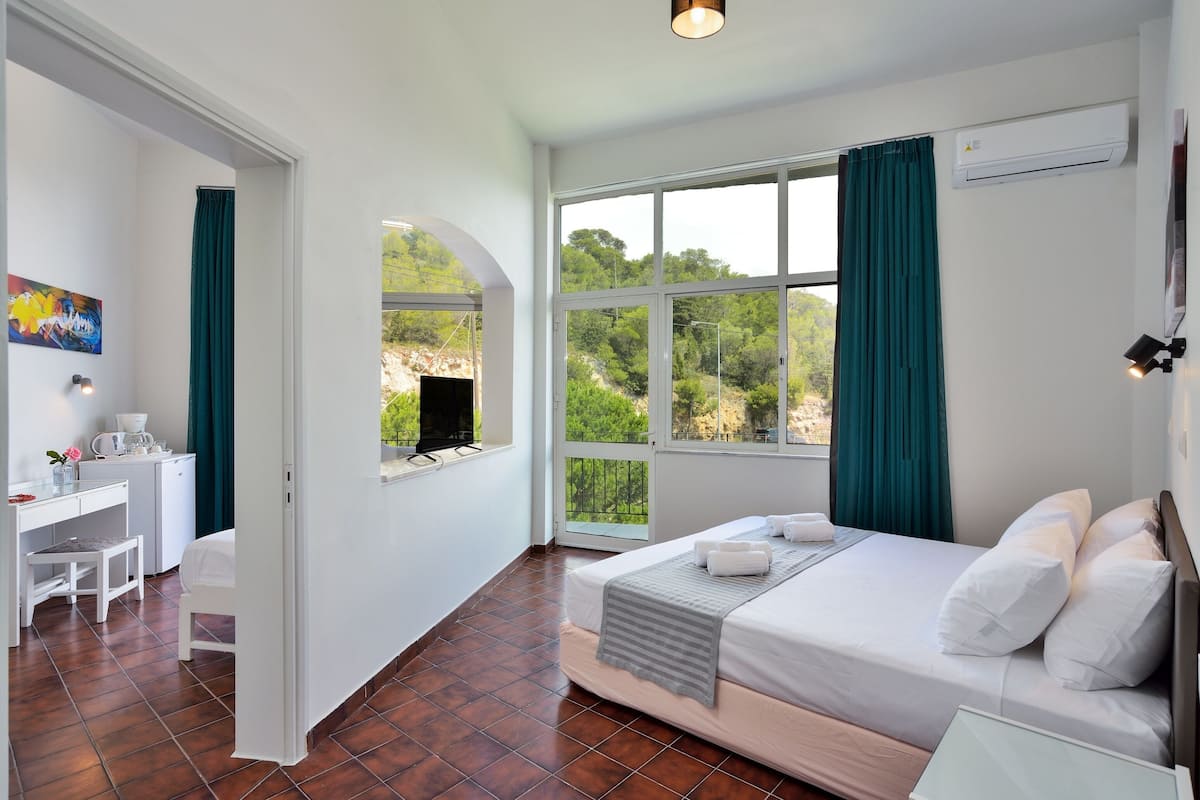 A hotel room with a bed, a desk, and a chair. There is a window with curtains, and an air conditioning unit on the wall.