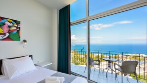 Ein Hotelzimmer mit einem großen Bett, Meerblick und einem Balkon mit Stühlen und einem Tisch.