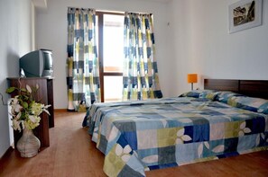 Een slaapkamer met een bed, gordijnen, een televisie op een kast en een vaas met bloemen.
