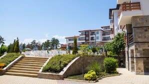 A multi-story hotel with a pool area, outdoor seating, and a staircase leading to the entrance. - Festa Gardenia Hills (Sunny Beach)