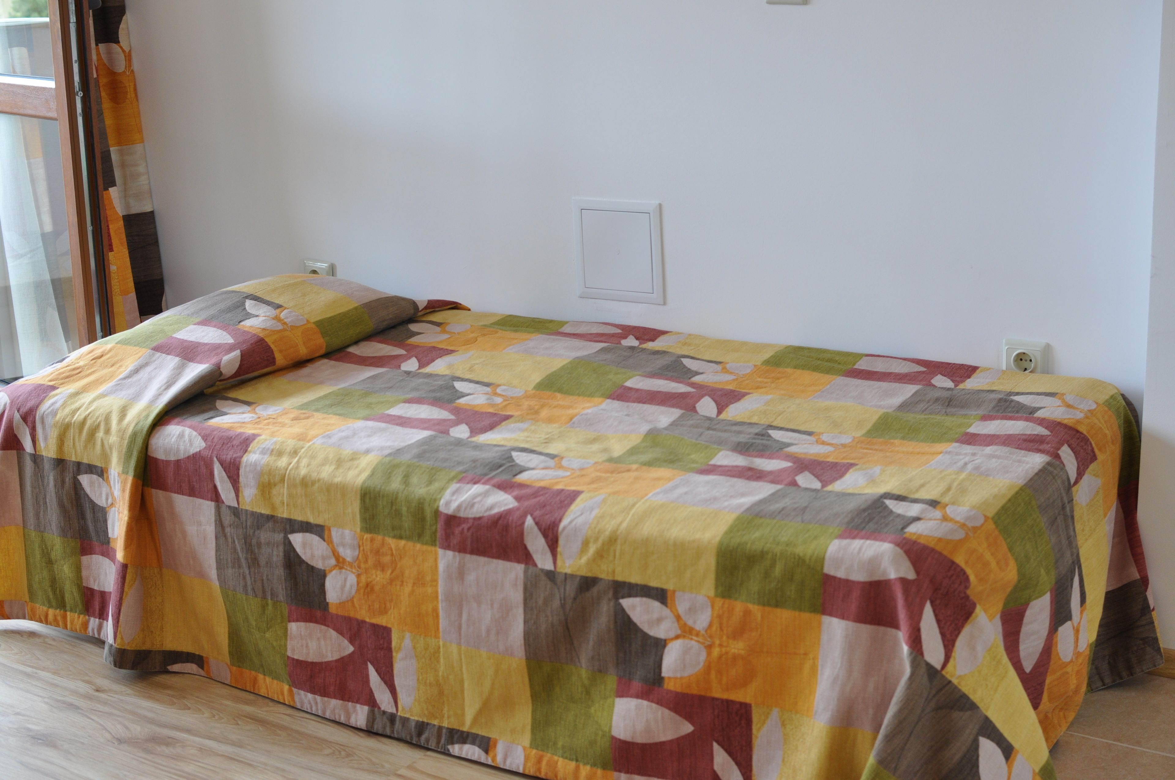 Una cama con un colcha colorida, una mesita de noche y un enchufe en la pared.