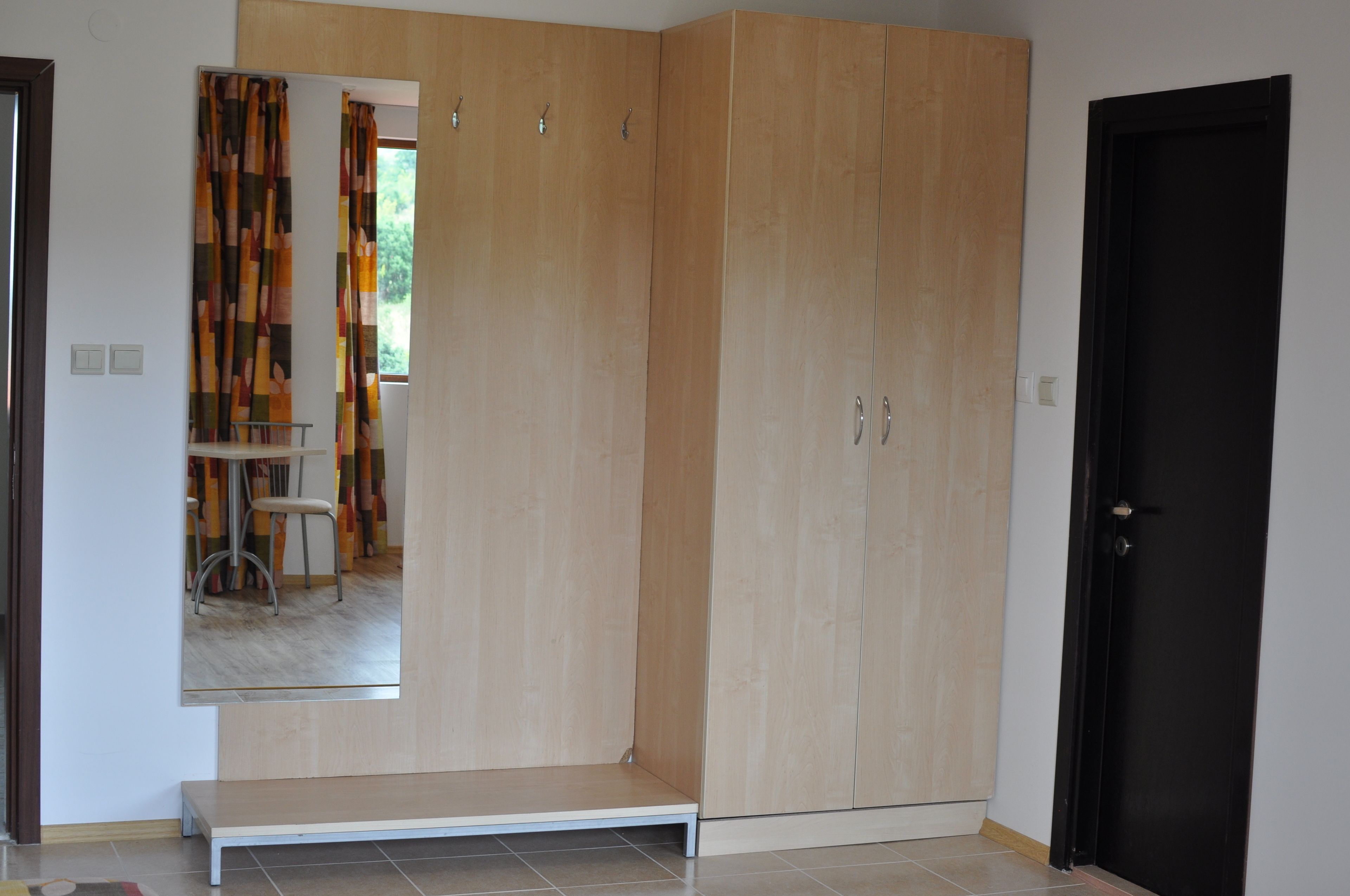 A room with a large wardrobe, a small table with a chair, and a door.