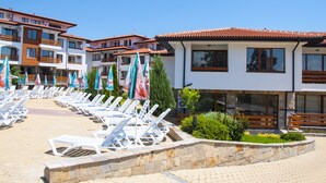 A hotel with multiple balconies, a pool area with sun loungers and umbrellas, and a well-maintained garden. - Festa Gardenia Hills (Sunny Beach)