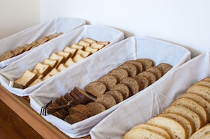 Een buffet met verschillende soorten brood en gebak, gerangschikt op wit doek bedekte schalen.
