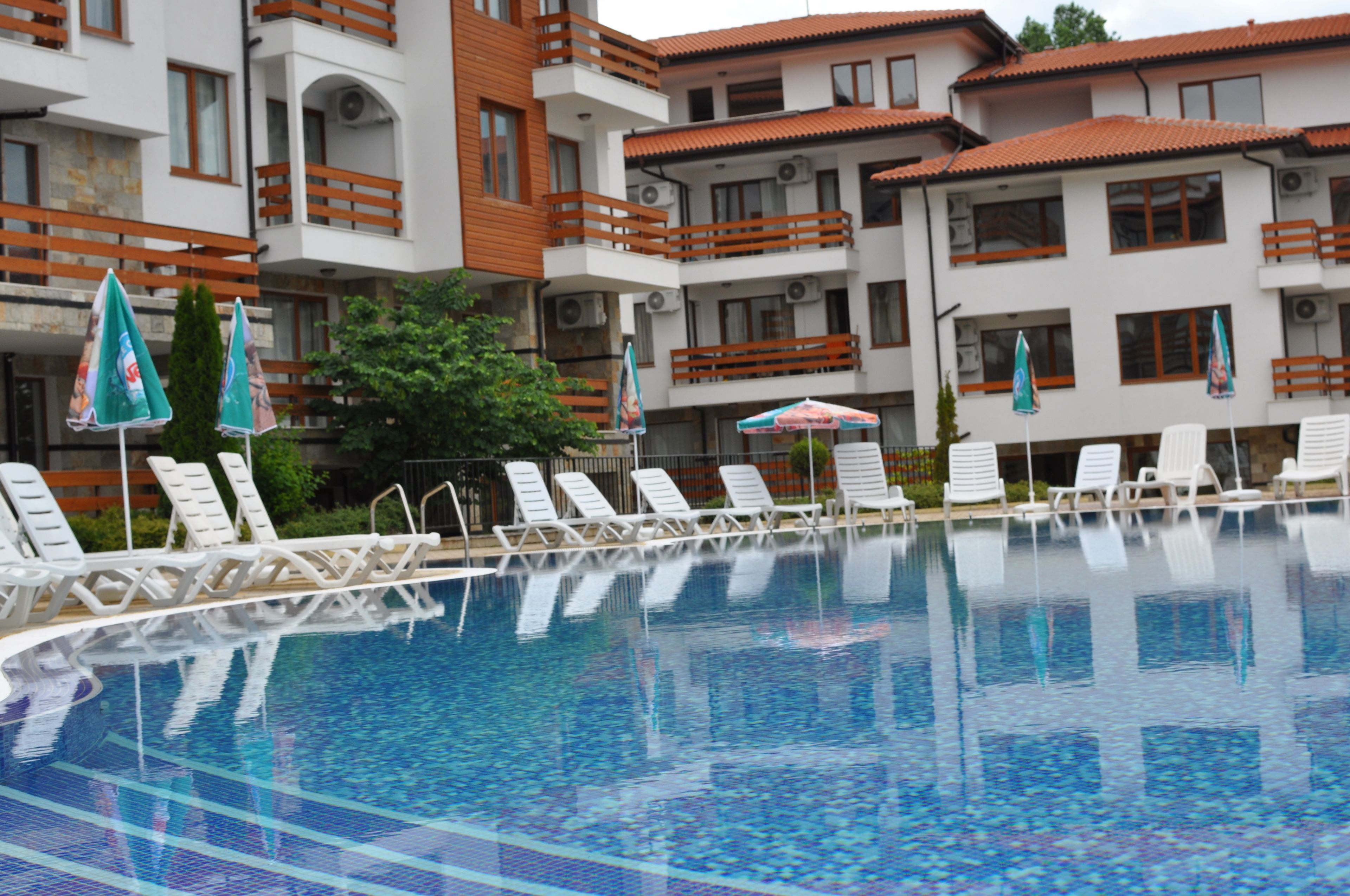 A swimming pool with white lounge chairs and umbrellas, surrounded by multi-story buildings with balconies.