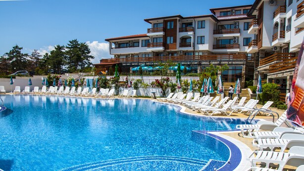 A large swimming pool with sun loungers and umbrellas, surrounded by a multi-story building with balconies. - Festa Gardenia Hills (Sunny Beach)