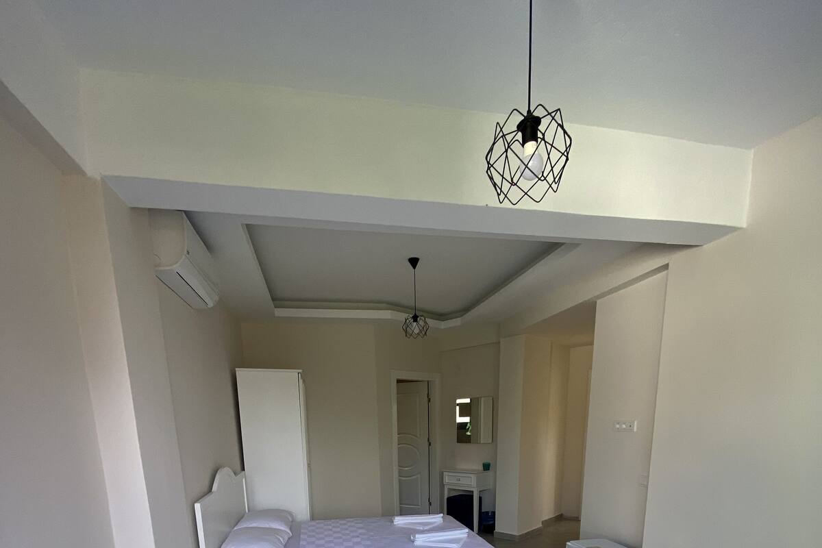 A hotel room with two beds, a ceiling light fixture, a small bedside table, and a mirror on the wall.