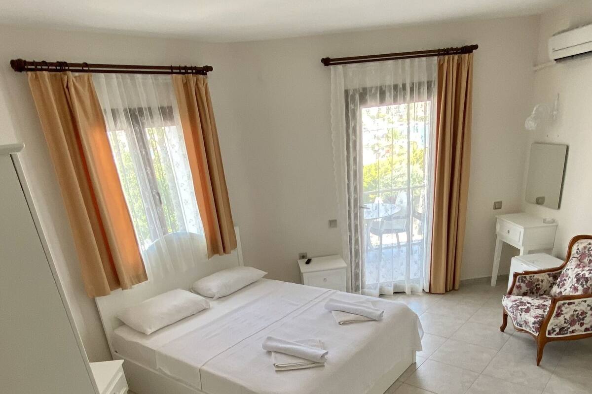 A hotel room with a large bed, a chair, a desk, and a window with curtains.