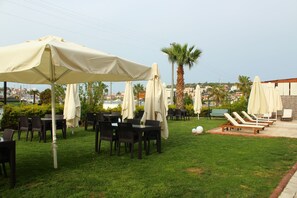 An outdoor seating area with tables and chairs, covered by umbrellas, and a poolside lounge with sun loungers. - Cilek Butik Otel (Cesme)