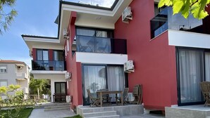 A modern two-story house with a red facade, large windows, and a well-maintained lawn. - Cilek Butik Otel (Cesme)