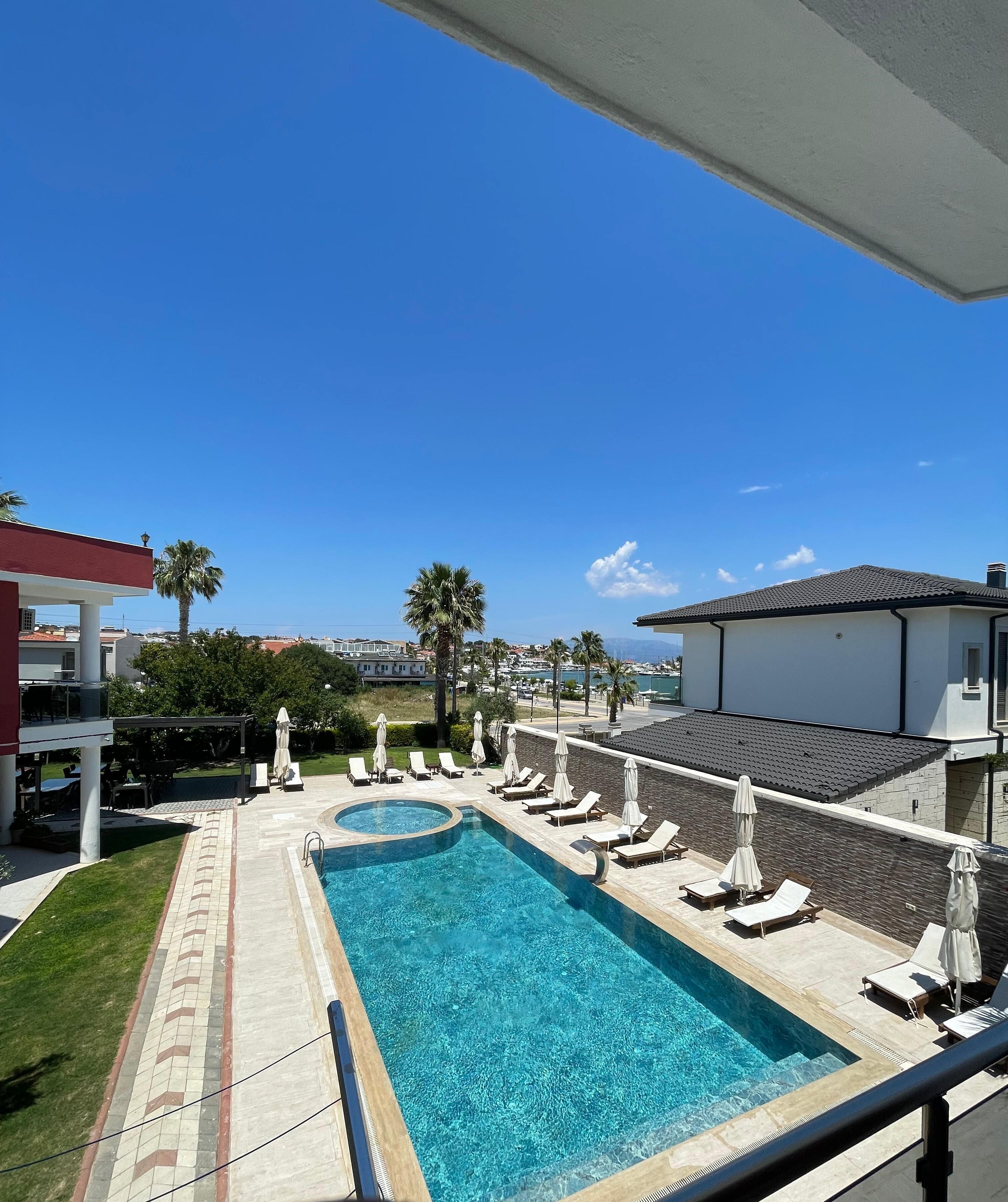 Ein Swimmingpool mit Liegestühlen und Sonnenschirmen, umgeben von Palmen und Gebäuden.