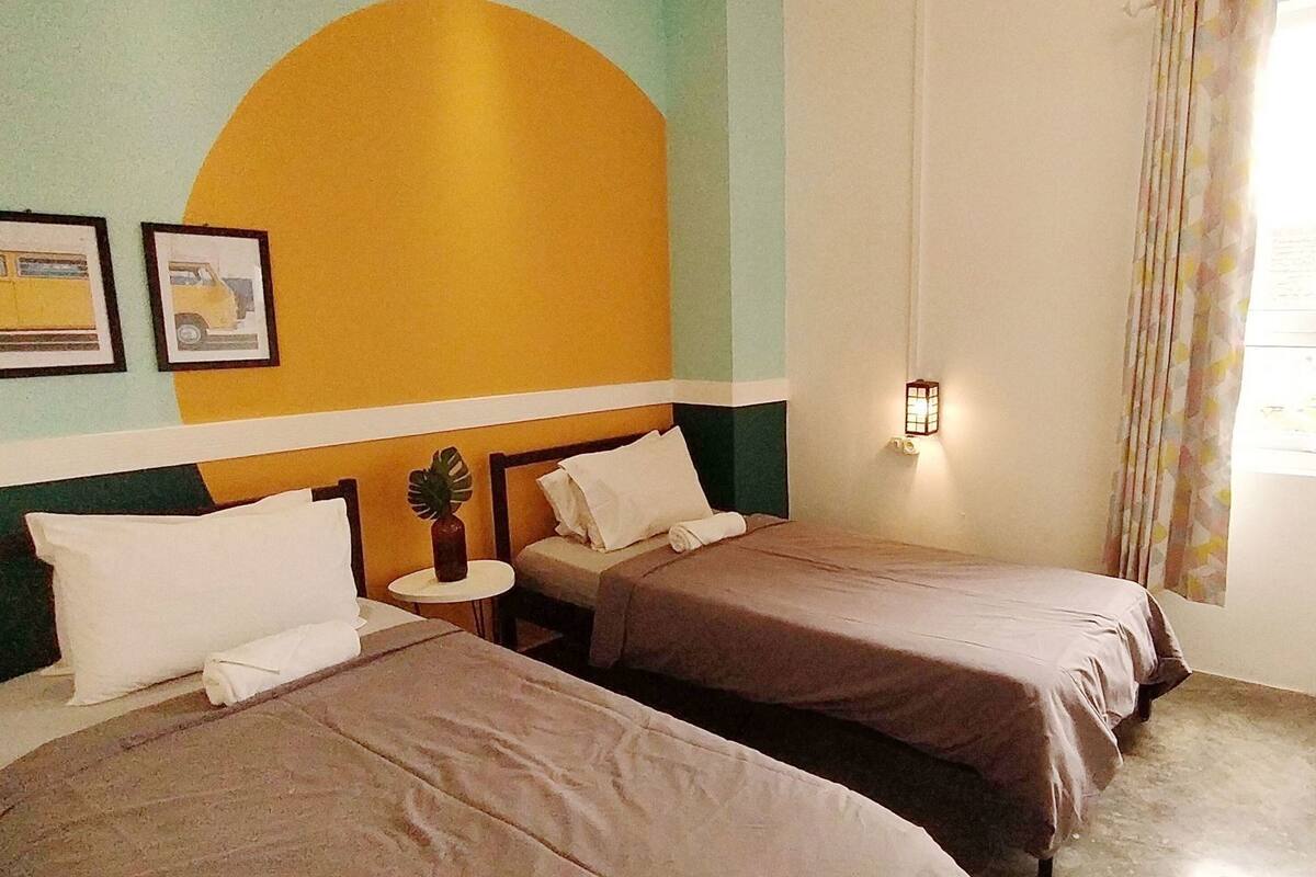 Una habitación con dos camas, una mesita redonda con una planta y una pared con un diseño circular grande.