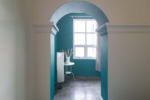 A narrow hallway with a teal wall, a white floor lamp, and a window with a curtain. - Wonderloft Hostel Kota Tua (Jakarta)