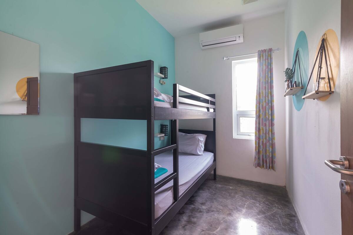 Dormitorio con literas, ventana, aire acondicionado y cortina.