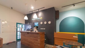A modern hostel reception area with a wooden counter, a clock, and a seating area. - Wonderloft Hostel Kota Tua (Jakarta)