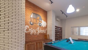 A billiards table with a pool cue and balls, a brick wall with a mural, and a wooden bench. - Wonderloft Hostel Kota Tua (Jakarta)