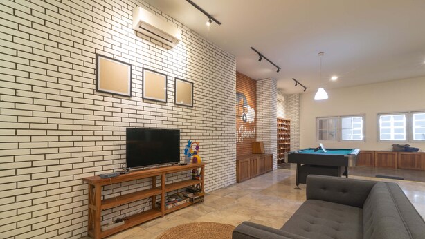 A living room with a brick wall, a television, a pool table, and a sofa. - Wonderloft Hostel Kota Tua (Jakarta)