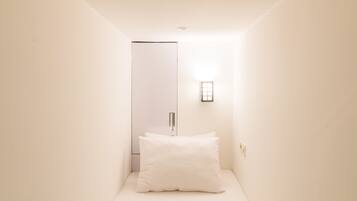 A minimalist bedroom with a single bed, a teal throw blanket, a bedside lamp, and a door with a mirror.