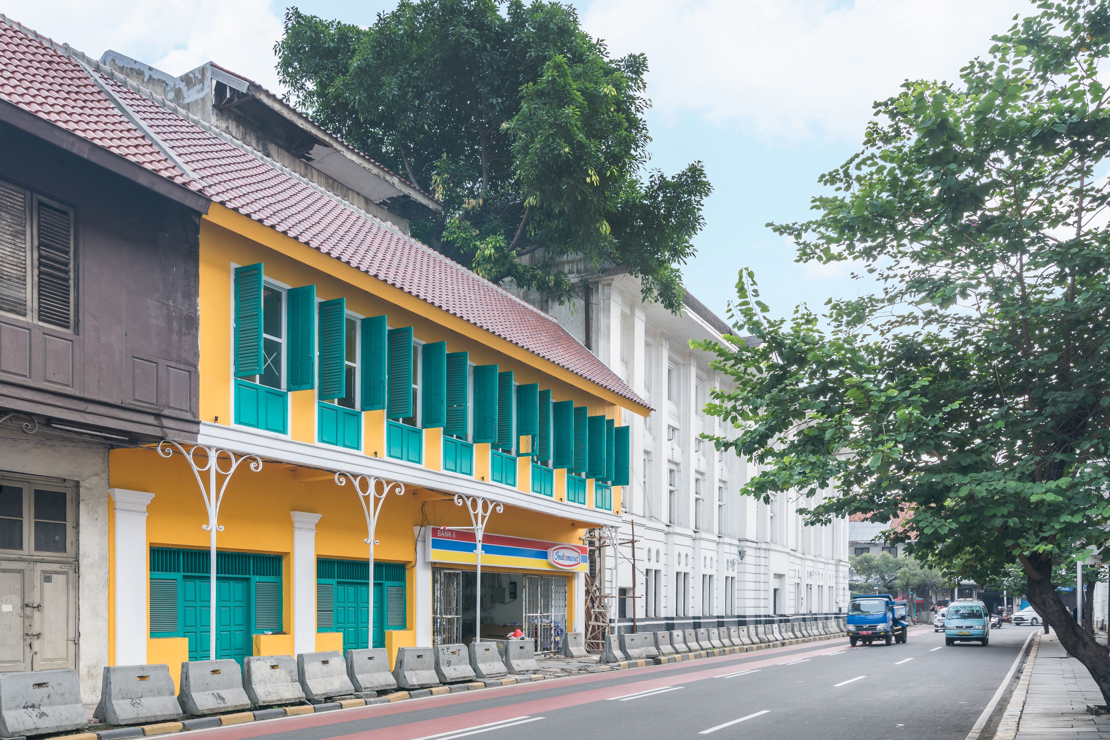 A two-story building with a yellow facade and green shutters, a signboard, and a sidewalk.