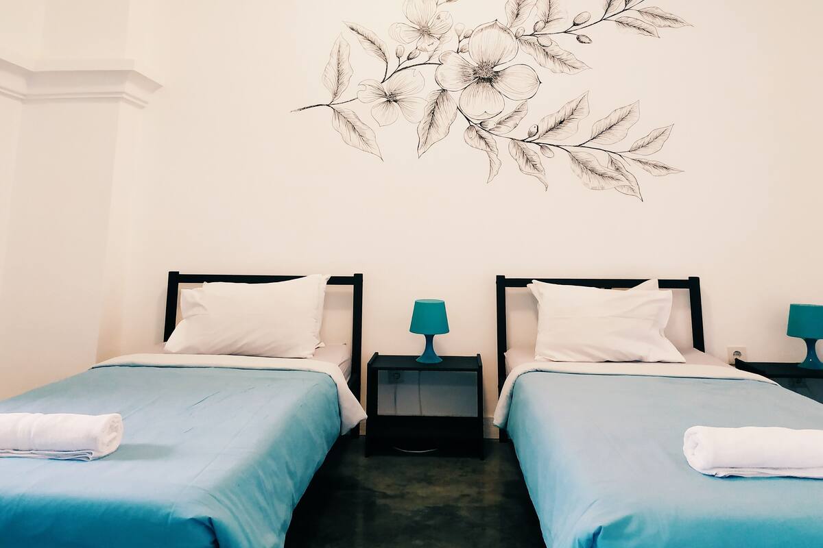 Habitación de hotel con dos camas, cada una con cubrecama azul y almohadas blancas, y una obra de arte en la pared sobre las camas.
