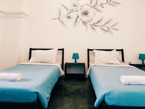 A hotel room with two beds, each with a blue bedspread and white pillows, and a wall art piece above the beds. - Wonderloft Hostel Kota Tua (Jakarta)