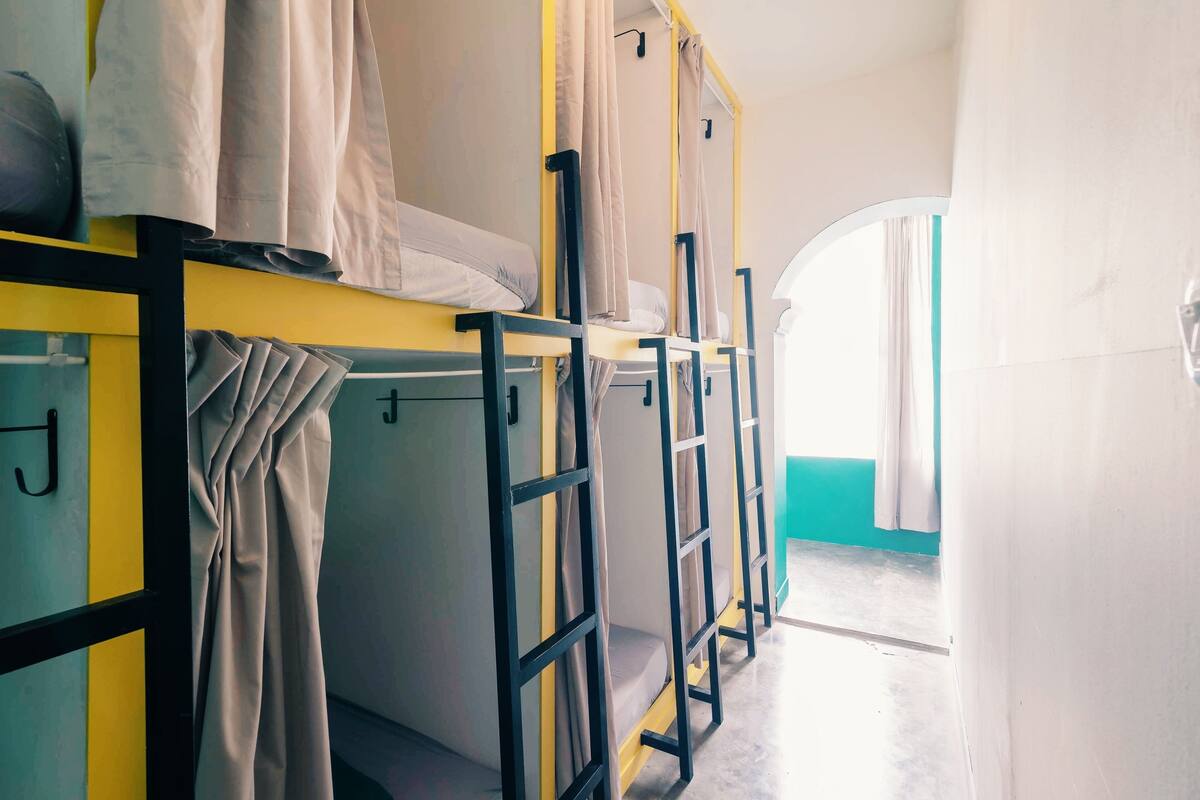 Varios camarotes con cortinas, suelo de baldosas y un vano que da a una habitación luminosa.