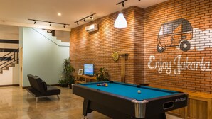 A pool table in a room with a brick wall, a staircase, and a sign that says "Enjoy Jakarta". - Wonderloft Hostel Kota Tua (Jakarta)