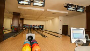 Une salle de bowling dotée de nombreuses pistes, d’une machine de retour des boules et d’écrans suspendus diffusant des publicités.