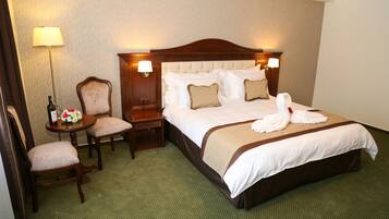 A hotel room with a large bed, two bedside lamps, a chair, a small table with a lamp, and a floral arrangement.