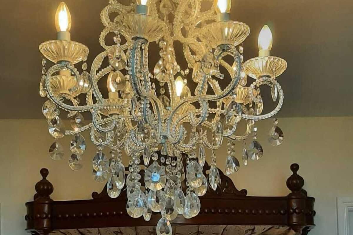 A bedroom with a large ornate chandelier, a wooden headboard with intricate carvings, and a plush dog bed.