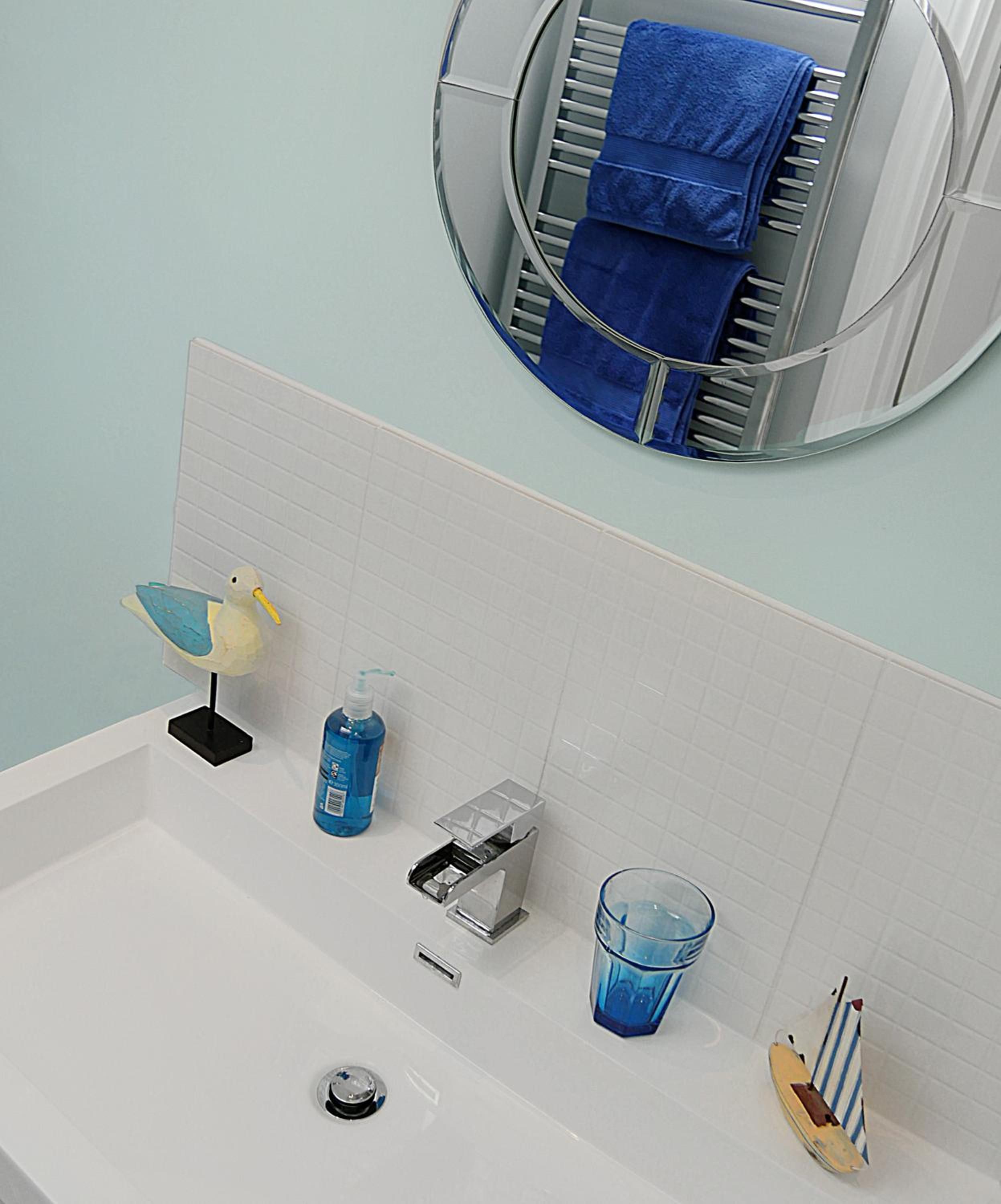 A bathroom with a bathtub, a hand soap dispenser, a glass of water, and a towel rack with a towel.