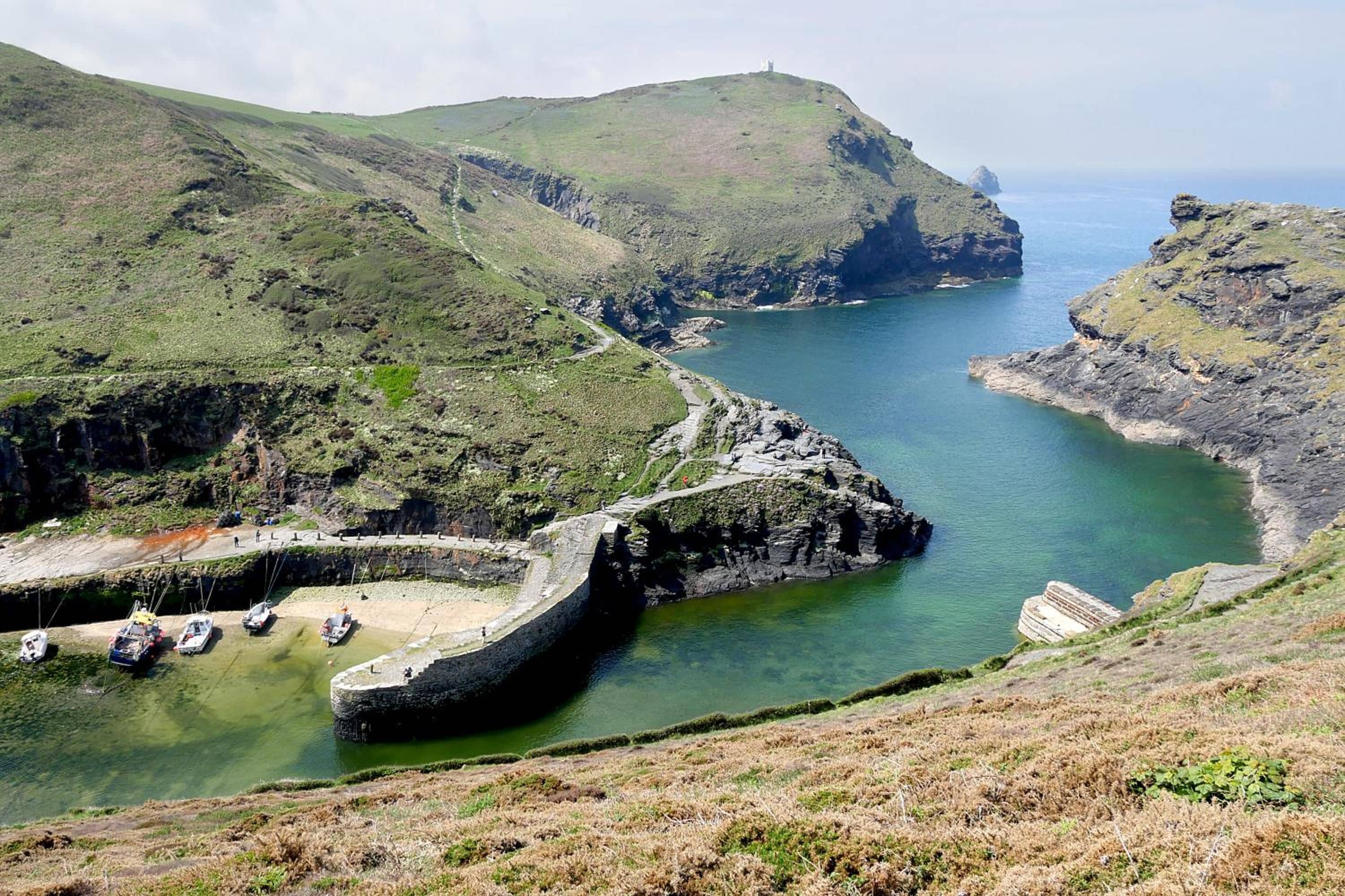 A coastal landscape with a sea wall, boats, and a rocky shoreline.
