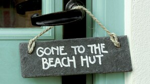 Un letrero de pizarra con una cuerda atada, colgado de un picaporte, que dice: "GONE TO THE BEACH HUT".